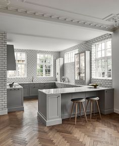 an empty kitchen with two stools in front of the island and windows on the wall