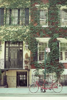 a red bike parked in front of a tall building with ivy growing on it's side