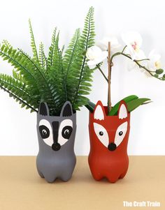 two ceramic vases with plants in them on a table next to each other, one has a fox and the other has a fern