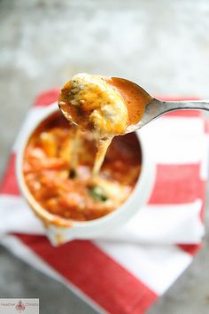 a spoon full of soup being lifted from a white bowl with red and white striped napkin