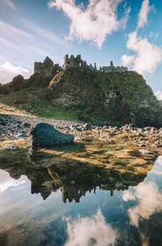 an old castle sits on top of a hill next to the water with clouds in the sky