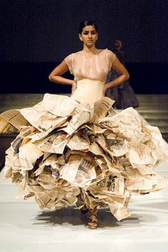 a woman is walking down the runway in a dress made out of books and paper