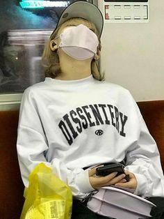 a woman sitting on a train with her cell phone in her hand and wearing a blindfold