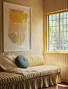 a striped couch in front of a window with a painting on the wall behind it