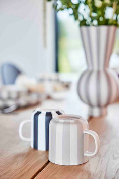 two coffee mugs sitting on top of a wooden table next to a vase with flowers in it