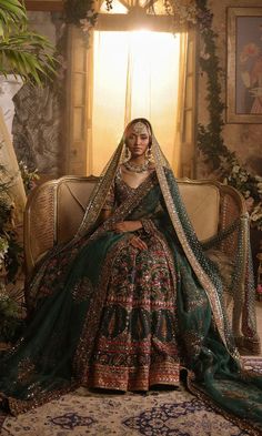 a woman sitting on top of a couch wearing a green and gold wedding dress with an elaborate veil