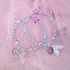 two bracelets with charms on them sitting on a pink netted cloth covered surface