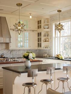 a kitchen with white cabinets and marble counter tops, an island in the middle is surrounded by four stools