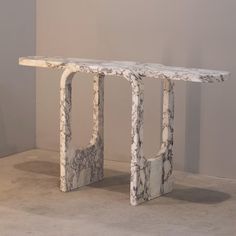 a white marble table with an abstract design on the top and bottom, against a gray wall