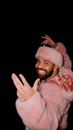 a man wearing a pink fur coat and holding his hands up in the air while smiling