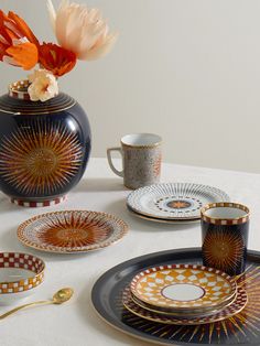 a table topped with plates and cups next to a vase filled with flowers on top of a white table cloth