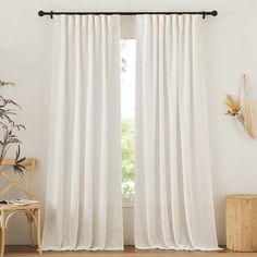 a white curtain hanging on the side of a window in front of a wooden chair