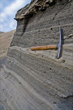 a knife stuck in the sand on top of a mountain side with a rock face behind it