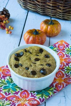 a white bowl filled with chocolate chip cookies on top of a colorful place mat next to two pumpkins