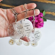 two heart shaped key chains are held by someone's hand with flowers in the background