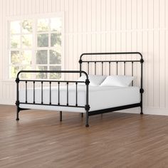 a black metal bed frame with white pillows and sheets on it in an empty room