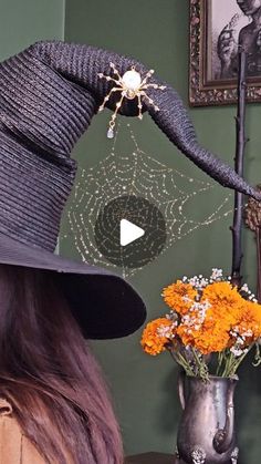 a woman wearing a black hat with spider web on it and flowers in a vase