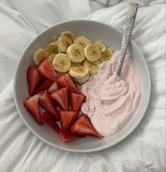 a white plate topped with sliced bananas and strawberries next to whipped cream in a bowl