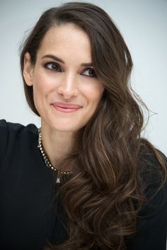 a woman with long brown hair wearing a black shirt and necklace smiling at the camera