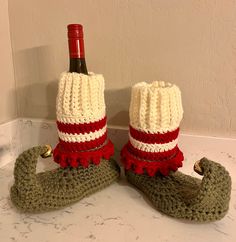 two crocheted boots with red and white trim, one holding a bottle of wine