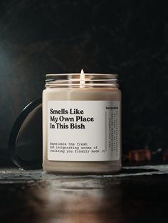 a candle sitting on top of a wooden table next to a black mug with the words smells like my own place in this dish