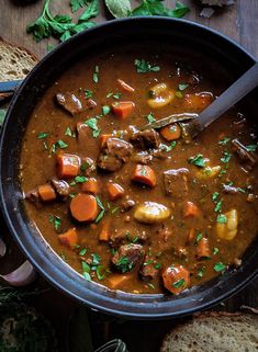 a bowl of stew with carrots, potatoes and bread