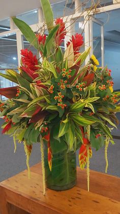 a green vase filled with red flowers on top of a wooden table in an office