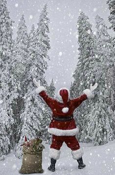 a man dressed as santa clause standing in the snow next to a bag of presents