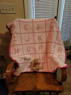 a teddy bear sitting on top of a wooden chair under a pink crocheted blanket