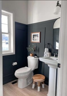 a white toilet sitting next to a sink in a bathroom under a window with blue walls