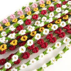 crocheted flowers are arranged in rows on a white surface, with green and red trimmings