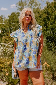 - Embrace feminine florals this season with this sweet top! - Unlined material with a colorful floral print - A ruffled v-notched neckline - A smocked upper bodice - Short flutter sleeves - A relaxed silhouette that ends in a rounded hemline Spring Ditsy Floral Print Blouse With Flutter Sleeves, Blue Floral Print Tops With Ruffle Sleeves, Spring Flutter Sleeve Blouse With Ditsy Floral Print, Blue Bohemian Blouse With Ruffle Sleeves, Bohemian Blue Blouse With Ruffle Sleeves, Floral Print Ruffle Sleeve Blouse For Vacation, Blue Flutter Sleeve Tops With Floral Print, Blue Floral Print Top With Flutter Sleeves, Blue Floral Print Tops With Flutter Sleeves