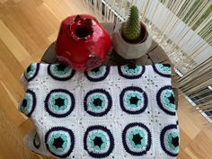 a crocheted table with a red vase and pot holder on it, sitting next to a cactus