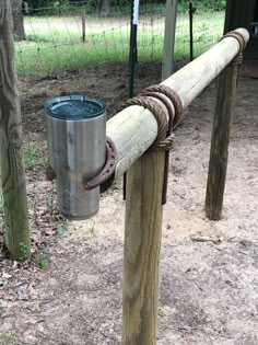 a metal bucket sitting on top of a wooden post next to a fence in the woods