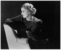 a black and white photo of a woman sitting in a chair with her hand on the arm