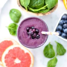 a smoothie with blueberries, oranges and spinach leaves on the side