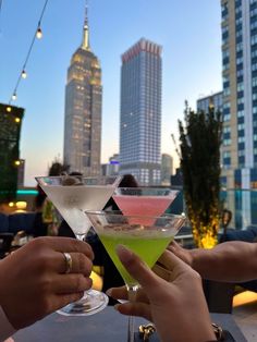 two people toasting with cocktails in front of the city's skyscrapers