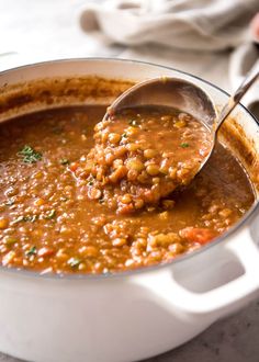 a ladle full of beans being spooned into a white pot filled with soup