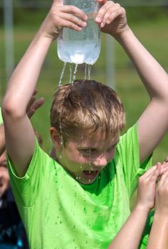 a young boy holding a water bottle over his head