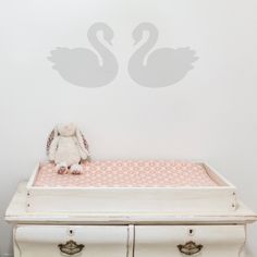 a stuffed animal sitting on top of a white dresser next to a swan wall decal