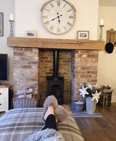 a person laying on a bed in front of a fireplace with a clock above it