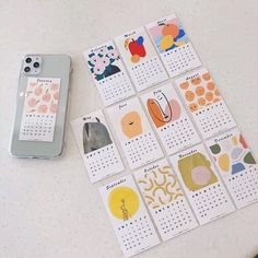 several calendars are placed next to a phone on a table with an iphone in the background