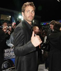 a man in a black suit and tie giving the thumbs up sign at an event