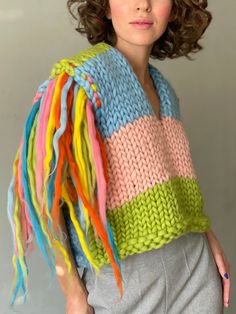 a woman wearing a multicolored knitted sweater with fringes on her shoulders