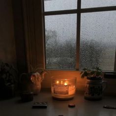 a candle sitting on top of a window sill in front of a rainy window