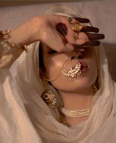 a woman in a white shawl holding her hands up to her face with jewelry on it