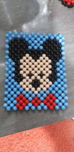 an image of a cross stitch bead pattern on a piece of metal foil with red, white and blue beads in the shape of a cartoon character