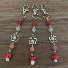 the charms are hanging from the chain on the wooden table with red and white beads