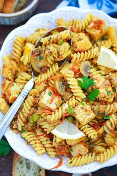 a white bowl filled with pasta and vegetables on top of a table next to bread