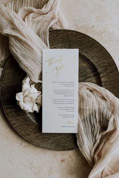 a menu card on a plate with white flowers in the middle and an unwoven scarf around it